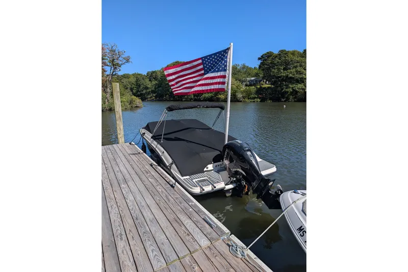 Slide: The Image of 2016 Sea Ray SPX 210 Outboard boat docked with American flag, calm water background. - 2