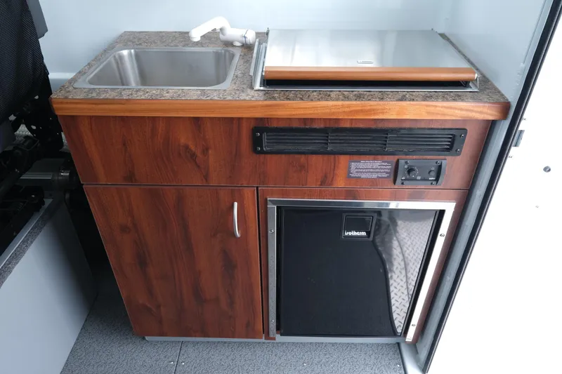 Slide: The Image of 2025 Hewescraft 240 Pacific Cruiser kitchenette with sink, stove, and compact fridge. - 17