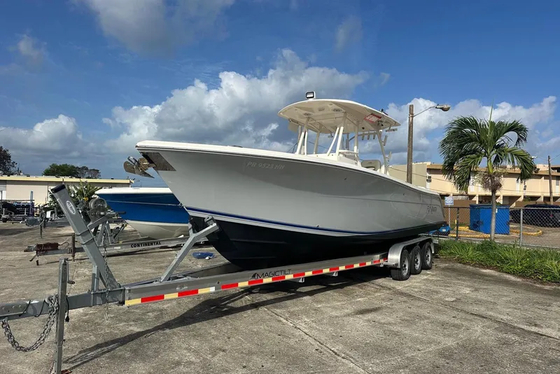 Slide: The Image of 2017 Cobia 296 Center Console boat on trailer, parked outdoors under cloudy sky. - 17