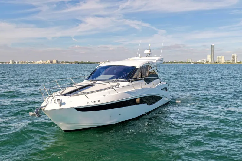 Slide: The Image of 2021 Galeon 425 HTS yacht cruising on open water with city skyline backdrop. - 6