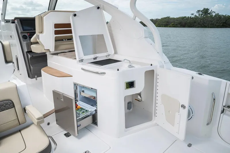 Slide: The Image of Manufacturer Provided Image: 2018 Pursuit DC 365 Dual Console boat interior with open storage compartments and mini fridge. - 8