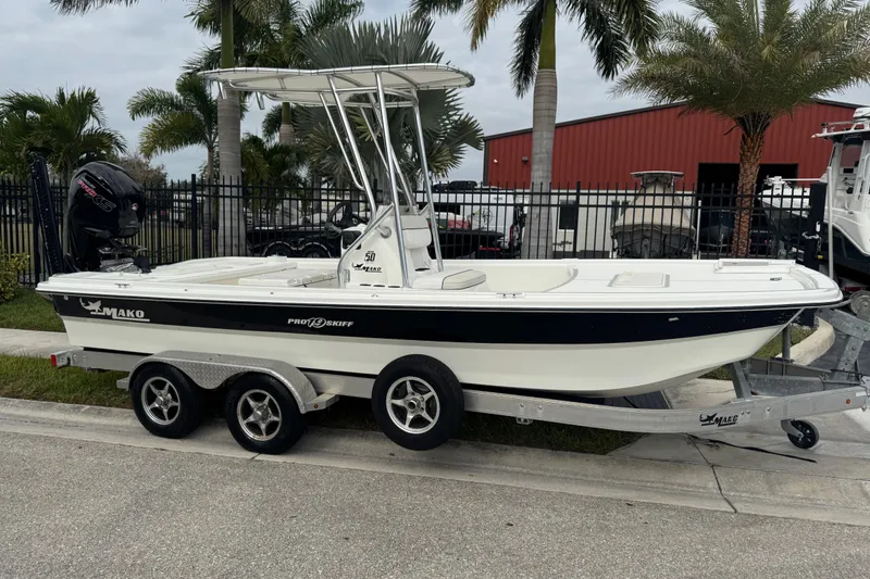 Slide: The Image of 2017 Mako Pro Skiff 19 CC boat on trailer, parked near palm trees. - 2