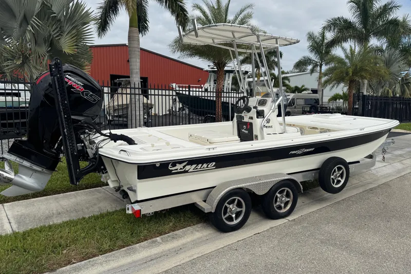 Slide: The Image of 2017 Mako Pro Skiff 19 CC boat on trailer, parked near palm trees. - 4