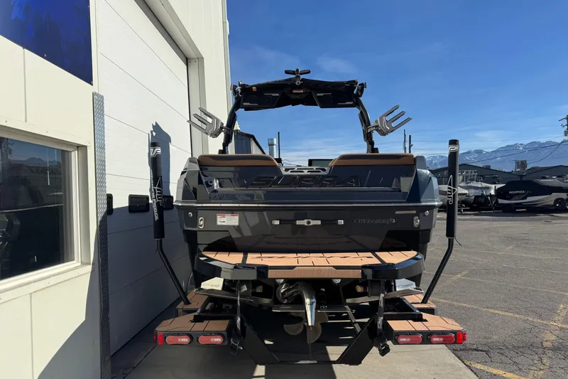 Slide: The Image of 2024 Supra SL 575 boat, rear view, parked outdoors near a building. - 2