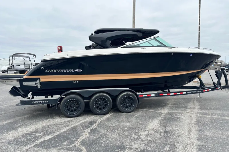 Slide: The Image of 2023 Chaparral 30 Surf boat on trailer, black and gold design, parked outdoors. - 3