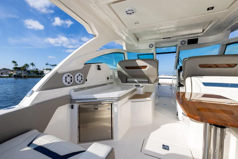 Slide: The Image of 2022 Tiara 34 LX luxury boat interior with seating and table, overlooking water and palm trees. - 10