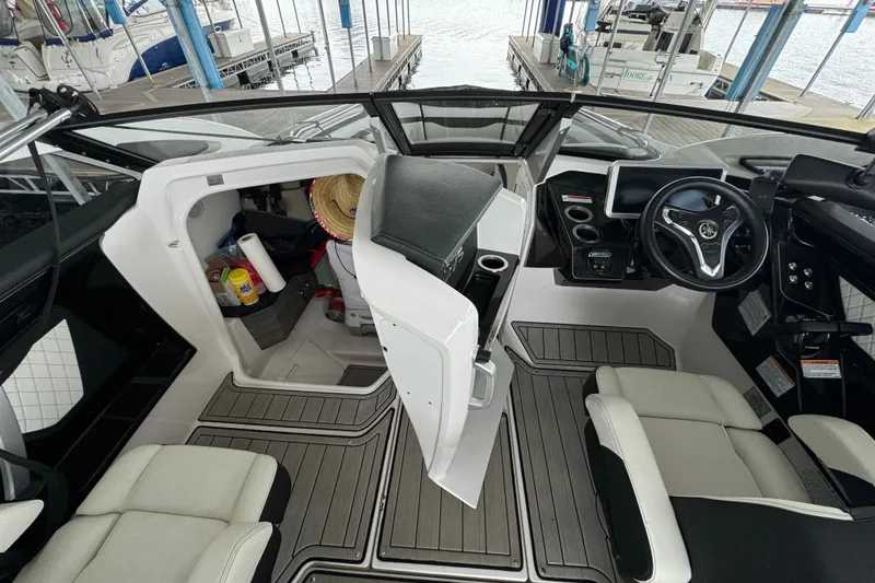 Slide: The Image of 2024 Yamaha Boats 275SD interior with helm, seating, and storage area at a marina. - 17
