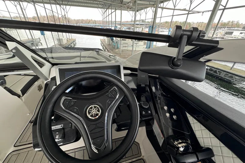 Slide: The Image of 2024 Yamaha Boats 275SD helm with steering wheel and control panel in marina setting. - 9
