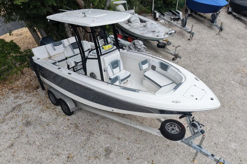 Slide: The Image of 2021 Robalo R230 Center Console boat on trailer, parked on gravel. - 2