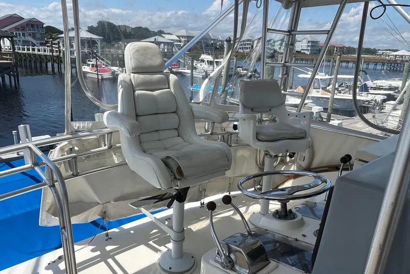 Slide: The Image of 1989 Topaz 44 Sportfisherman boat interior with marina view, featuring white seating and navigation equipment. - 8