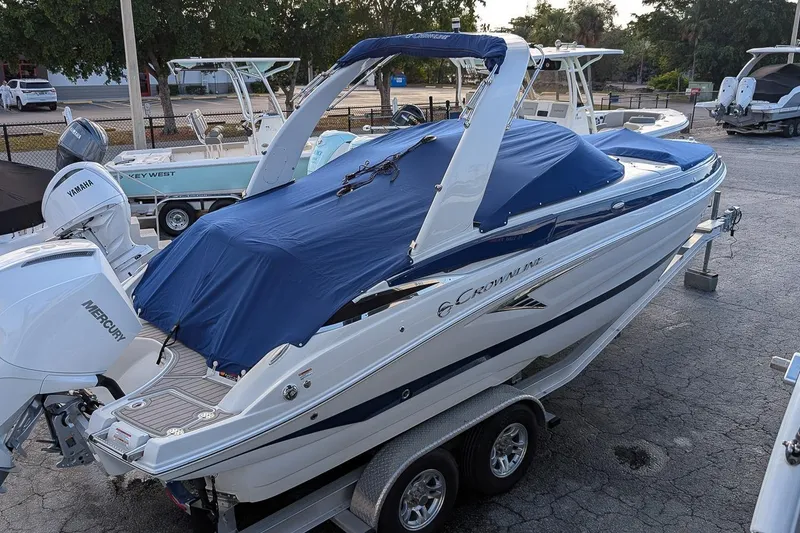 Slide: The Image of 2022 Crownline 260 XSS boat with blue cover on trailer, parked outdoors. - 17