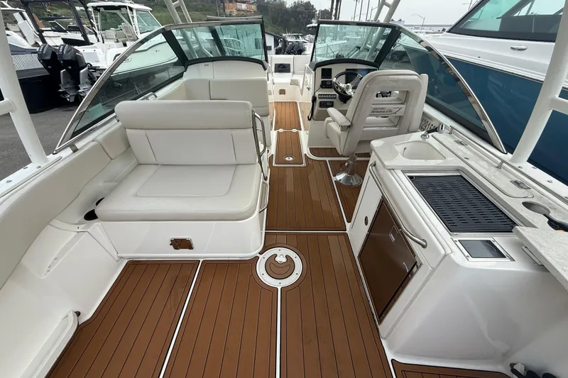 Slide: The Image of 2018 Boston Whaler 270 Vantage interior with seating, helm, and kitchenette on teak flooring. - 7