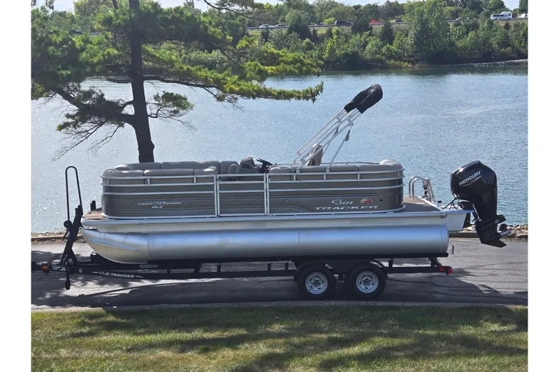 The Image of 2024 Sun Tracker Party Barge 20 DLX pontoon boat on trailer by a lake. - 0