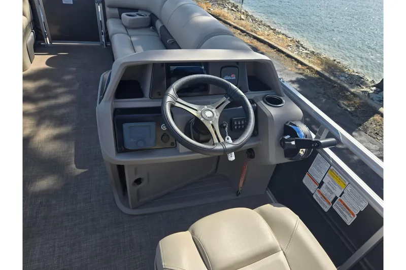 Slide: The Image of 2024 Sun Tracker Party Barge 20 DLX helm with steering wheel and controls, near water. - 21