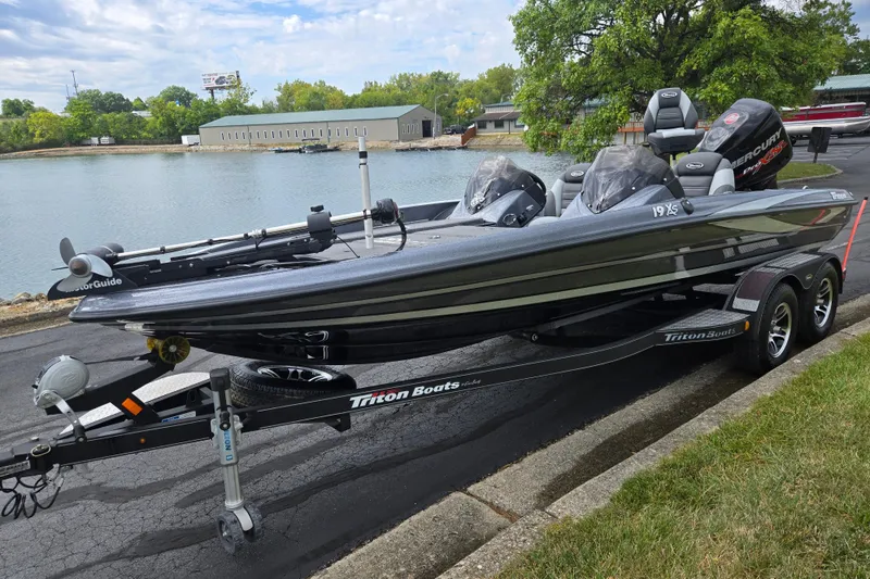 Slide: The Image of 2014 Triton 19XS boat on trailer by a lake, featuring dual seats and Mercury engine. - 10