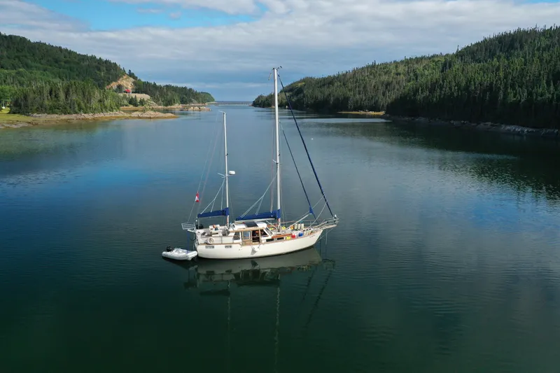 Slide: The Image of Sailboat Nauticat 38 (1987) anchored in a serene, forested bay under a cloudy sky. - 64
