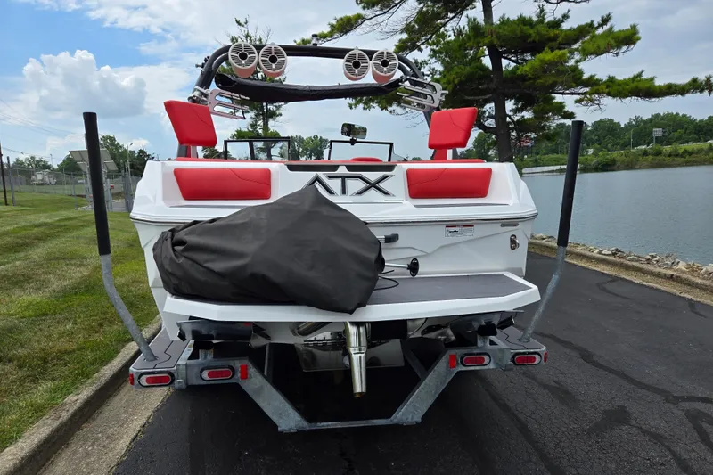 Slide: The Image of 2022 ATX Surf Boats 20 Type-S, rear view, parked near a lake with red seats. - 2