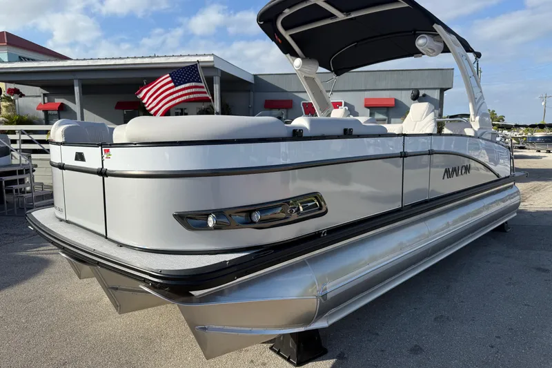The Image of 2026 Avalon 2385 Catalina Quad Lounger Tri Toon boat with American flag, parked outdoors. - 1