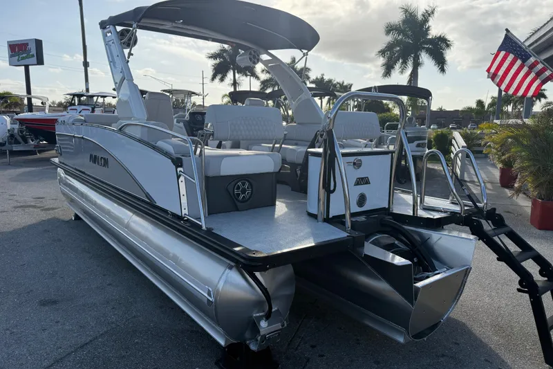 Slide: The Image of 2026 Avalon 2385 Catalina Quad Lounger Tri Toon boat, parked outdoors with American flag. - 12