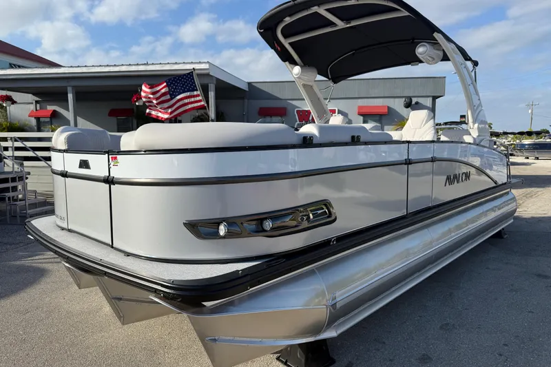 Slide: The Image of 2026 Avalon 2385 Catalina Quad Lounger Tri Toon boat with American flag, docked under blue sky. - 3