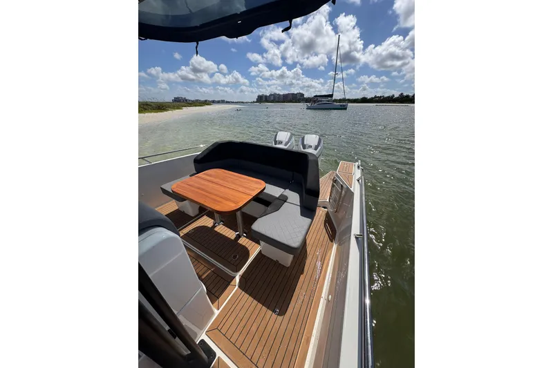 Slide: The Image of Nimbus T9 2021 boat with seating area, wooden table, and scenic waterfront view. - 12