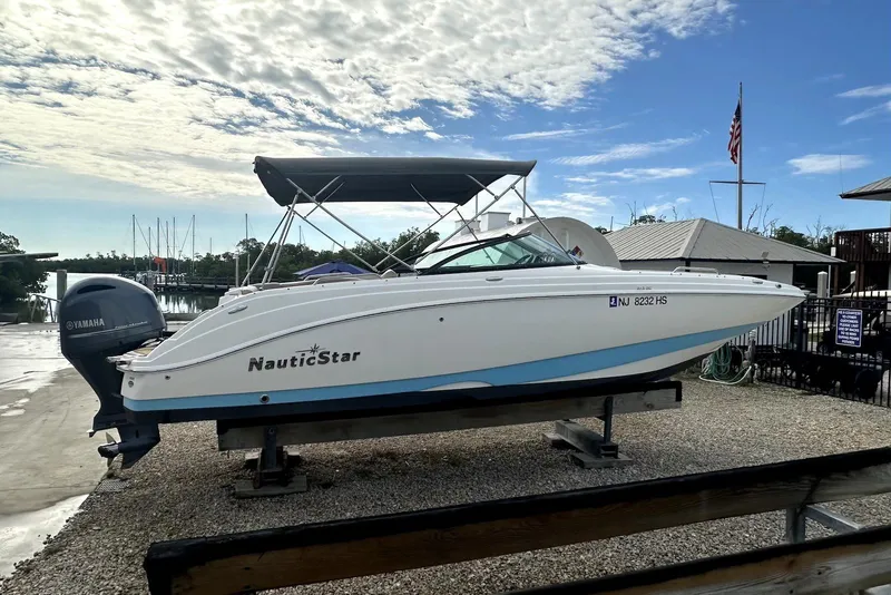 The Image of 2022 NauticStar 243 DC boat on a lift with Yamaha engine, marina background. - 0