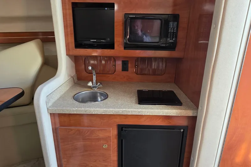 Slide: The Image of 2005 Rinker 300 Express Cruiser kitchenette with sink, microwave, and compact fridge. - 22