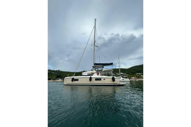 Slide: The Image of 2019 Lagoon 42 catamaran anchored in calm waters, with scenic background. - 4
