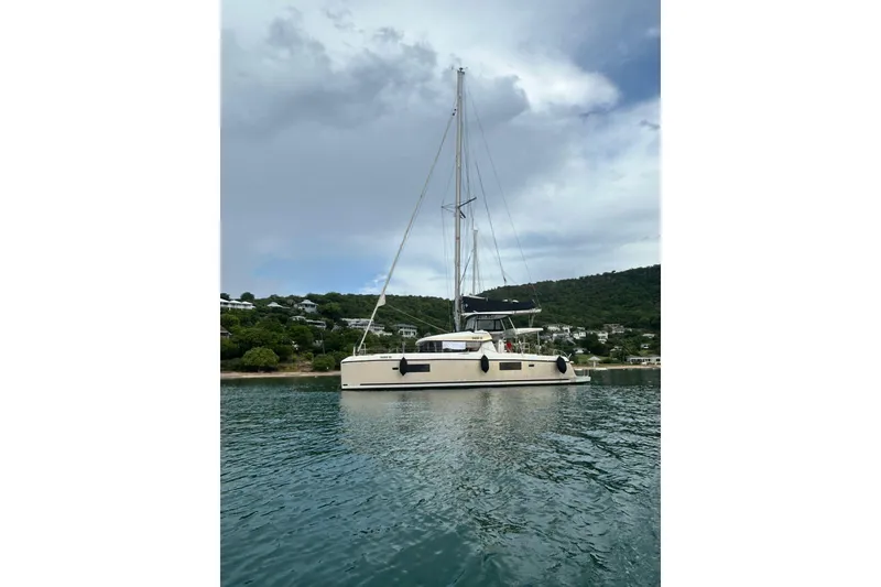 Slide: The Image of 2019 Lagoon 42 catamaran anchored in serene waters with lush hillside backdrop. - 67