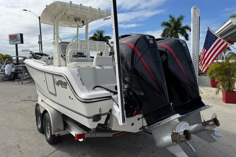 Slide: The Image of 2022 Mako 234 Center Console boat with dual engines, parked outdoors near American flag. - 9