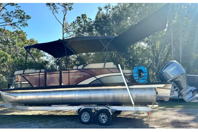 The Image of 2023 Sylvan L5 CLZ pontoon boat on trailer with Yamaha motor, parked outdoors. - 0