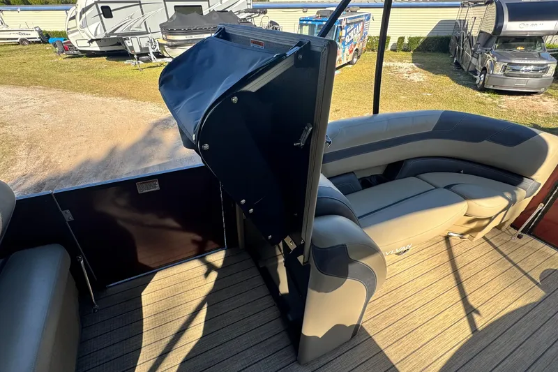 Slide: The Image of 2023 Sylvan L5 CLZ boat interior with seating and storage, parked near RVs. - 15
