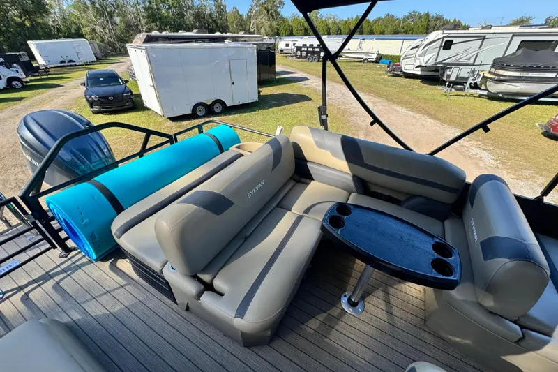 Slide: The Image of 2023 Sylvan L5 CLZ pontoon boat interior with seating and table, parked near trailers. - 8