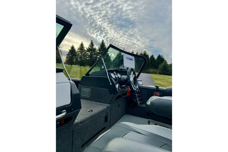 Slide: The Image of 2021 Lund 2175 Pro-V boat interior with steering console, under a cloudy sky. - 11