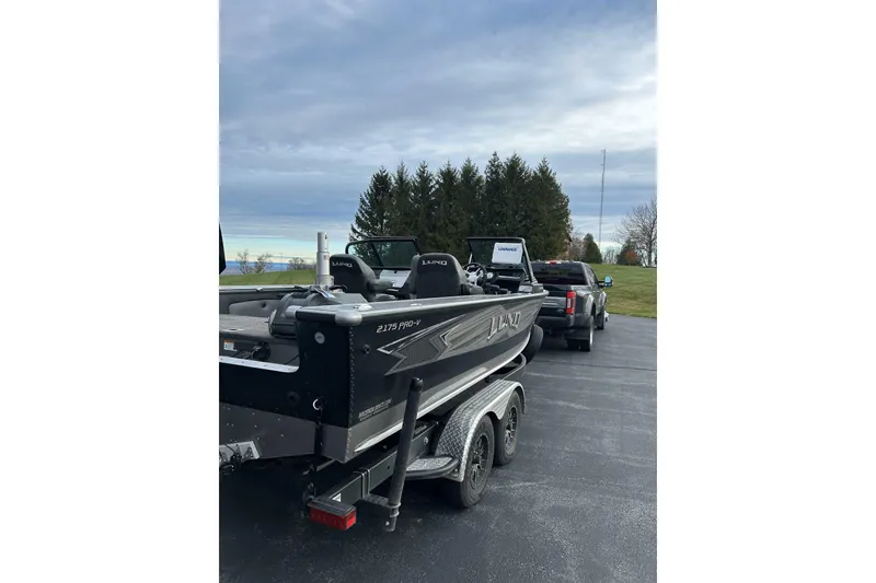 Slide: The Image of 2021 Lund 2175 Pro-V boat on trailer, parked on driveway under cloudy sky. - 4