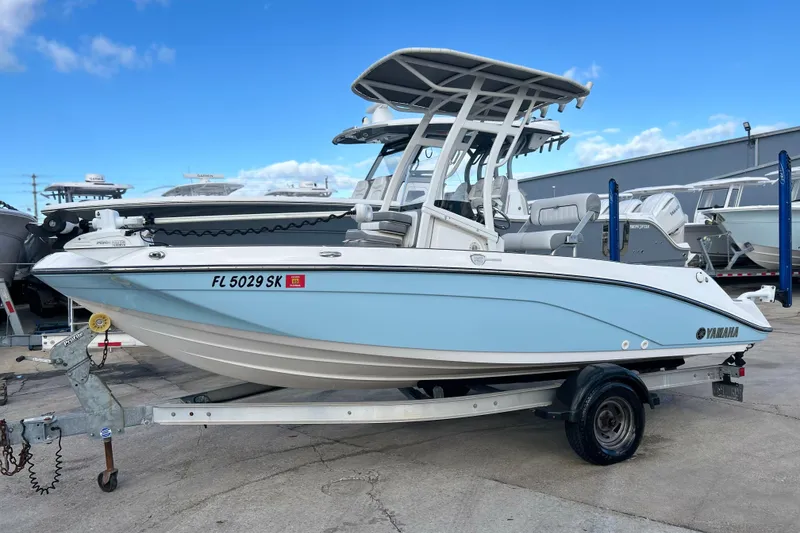 Slide: The Image of 2019 Yamaha Boats 190 FSH Sport on trailer, light blue hull, parked outdoors. - 2