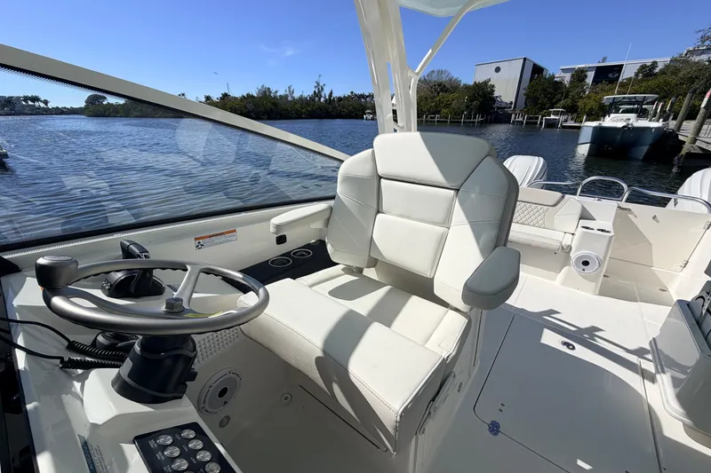 Slide: The Image of 2026 World Cat 325 DC boat interior with steering wheel and seating, docked by a scenic waterfront. - 14