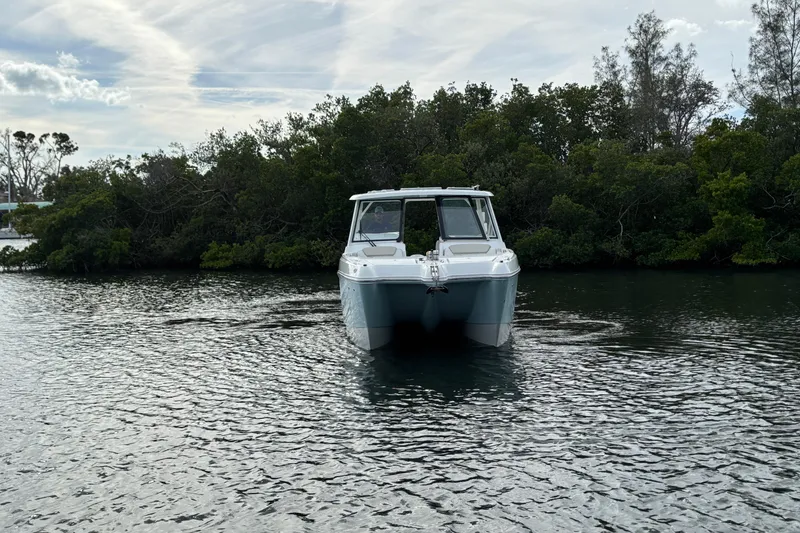 Slide: The Image of 2026 World Cat 325 DC boat on calm water with lush greenery background. - 2