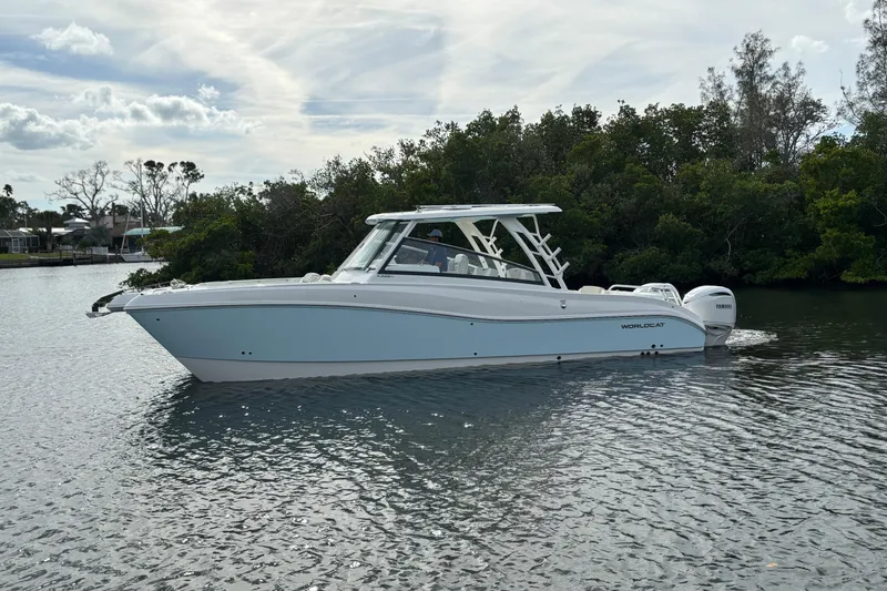 Slide: The Image of 2026 World Cat 325 DC boat on calm water, surrounded by lush greenery. - 5