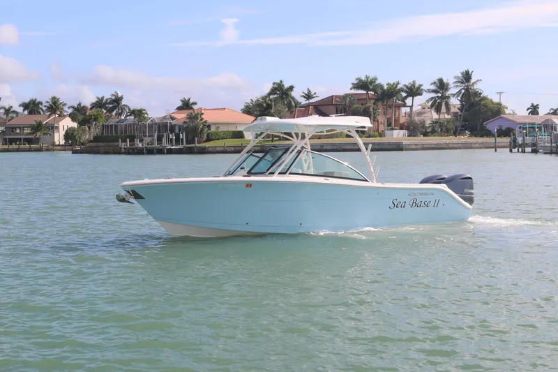Slide: The Image of 2019 Cobia 280 Dual Console boat cruising on a sunny day near waterfront homes. - 2