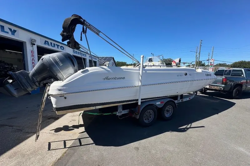 Slide: The Image of 2019 Hurricane SunDeck 237 OB boat on trailer, parked near auto service shop. - 1