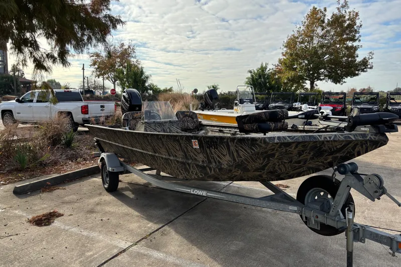 Slide: The Image of 2017 Lowe Roughneck 1860SC boat on trailer in parking lot, surrounded by trees and vehicles. - 1