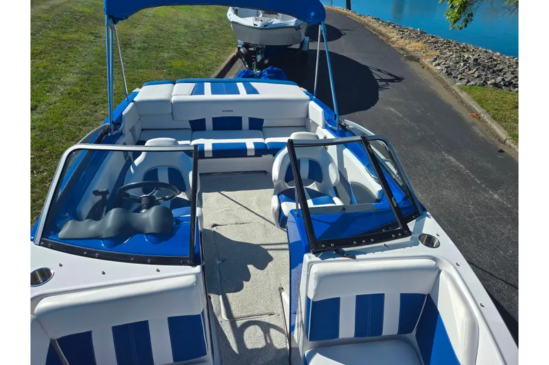 Slide: The Image of 2013 Glastron GT 205 boat with blue and white interior, parked near a lake. - 21