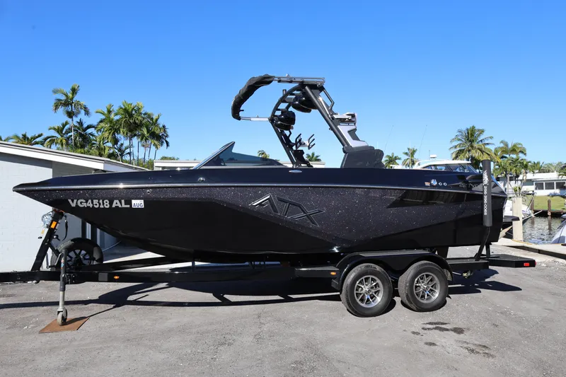 Slide: The Image of 2025 ATX Surf Boats 22 Type-S on trailer, sleek black design, parked near palm trees. - 2