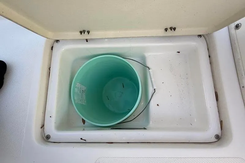 Slide: The Image of Open storage compartment on 2019 NauticStar 25 XS boat with a green bucket inside. - 26