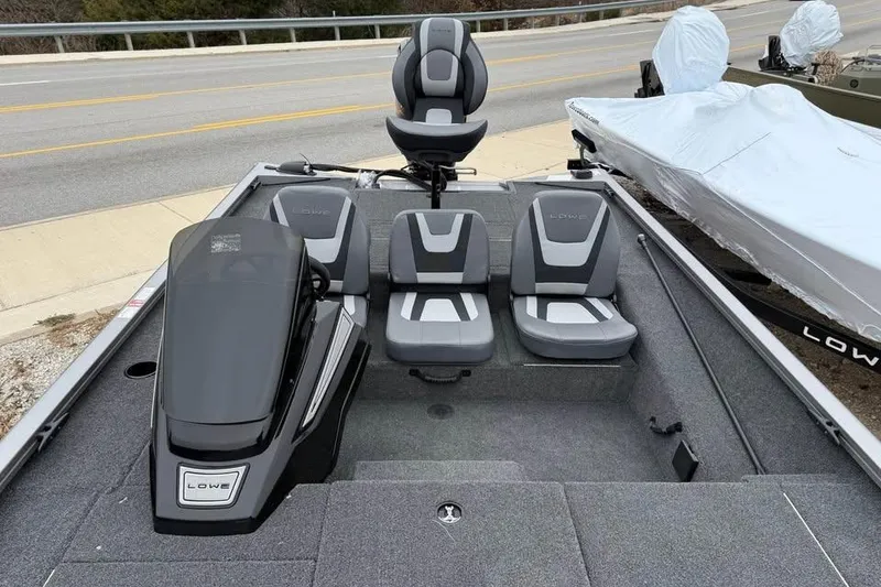 Slide: The Image of 2026 Lowe Stinger 195 Bass boat interior with gray seating and console, parked near a road. - 14