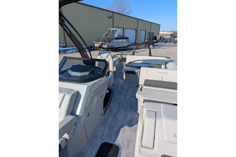 Slide: The Image of 2026 Sylvan G5 CLZ boat interior with modern seating and dashboard, parked outdoors. - 6