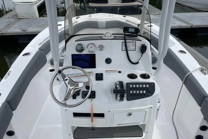 Slide: The Image of 2024 NauticStar 222L Offshore boat dashboard with steering wheel and controls at marina. - 4
