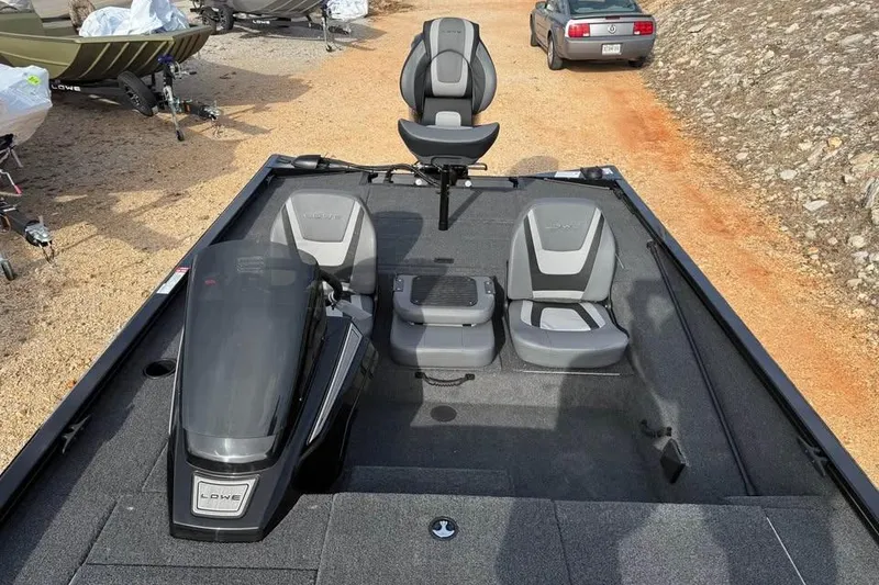 Slide: The Image of 2026 Lowe Stinger 195 Bass boat interior with seating and motor, parked on gravel. - 13