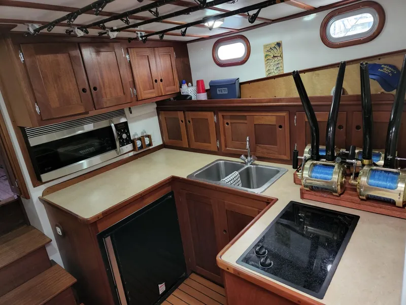 Slide: The Image of 2003 Wesmac Flybridge kitchen with wooden cabinets, dual sink, and fishing reels. - 48